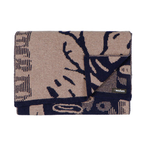 Flatlay of a jacquard knit scarf in dark indigo blue and beige. The scarf has a figurative pattern resembling trees in a forest.