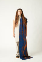 Load image into Gallery viewer, Wide shot of a young woman with a scarf draped over her shoulder. She&#39;s wearing a neutral light beige outfit and black shoes. The knit scarf is blue and brown with details in copper and gold.
