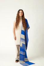 Load image into Gallery viewer, Wide shot of a young woman with a knit scarf draped over the shoulder. She&#39;s wearing a neutral toned outfit and black shoes. Packhshot of a jacquard knit scarf in cobalt blue and beige. The scarf has an abstract geometric bitmap pattern.
